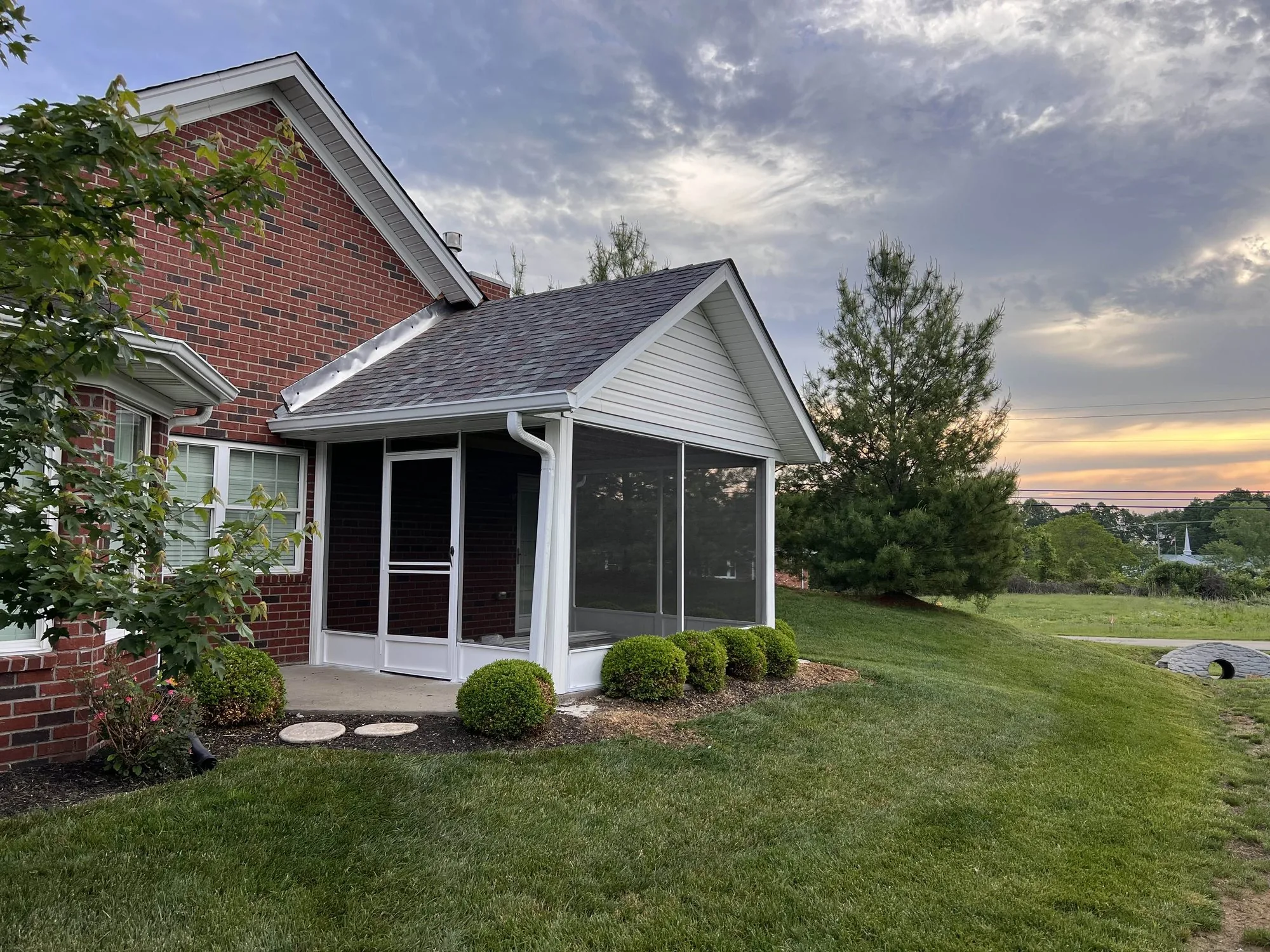 A screened porch addition on a brick home at sunset, seen across the back lawn.