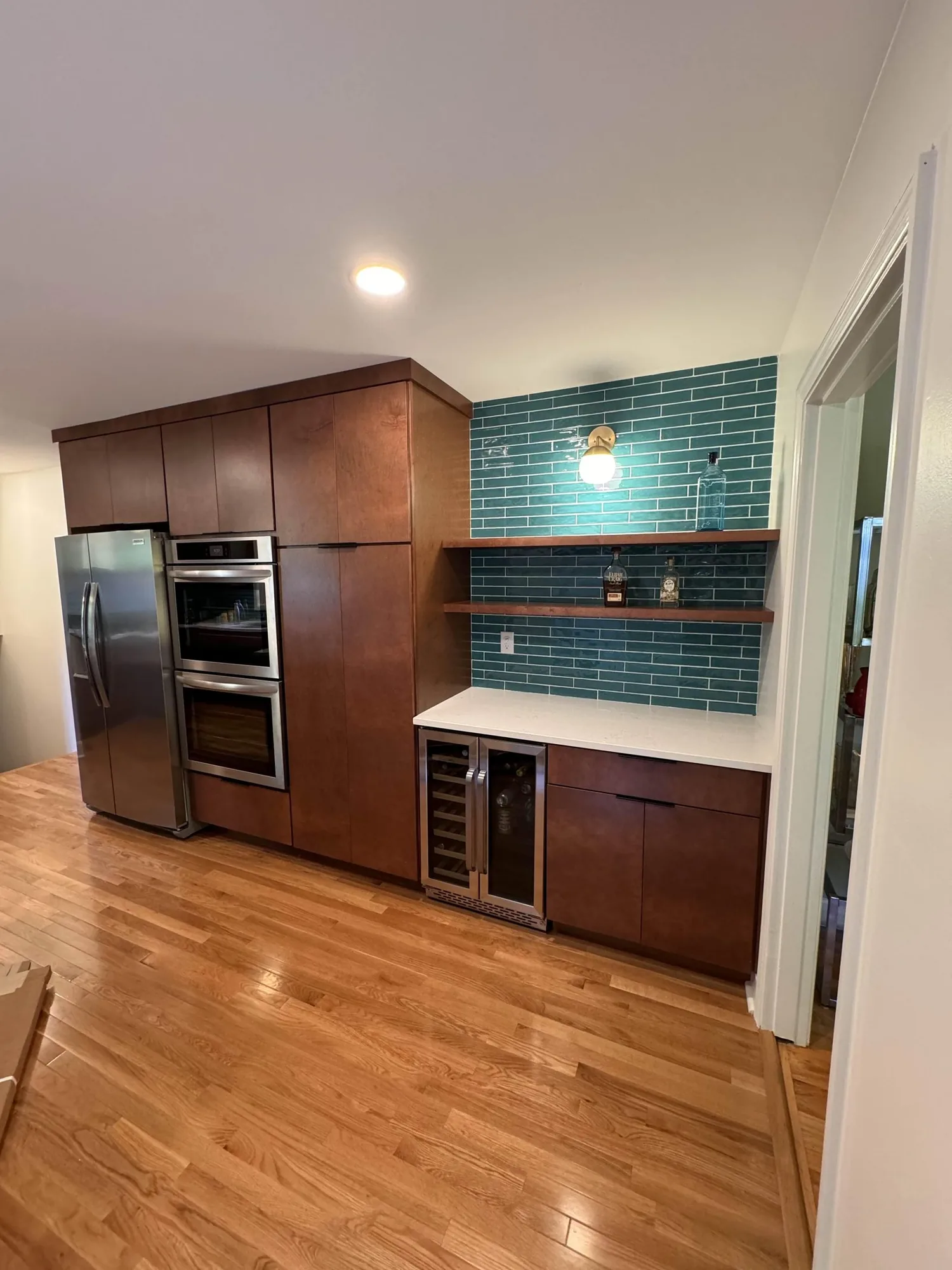 A remodeled kitchen with dark wood cabinetry, a teal tile backsplash and stainless appliances.